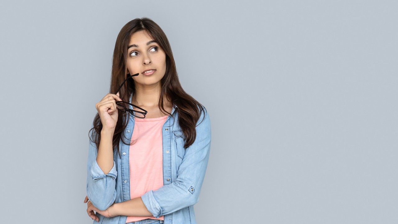 Curious young adult indian woman standing isolated on grey background.