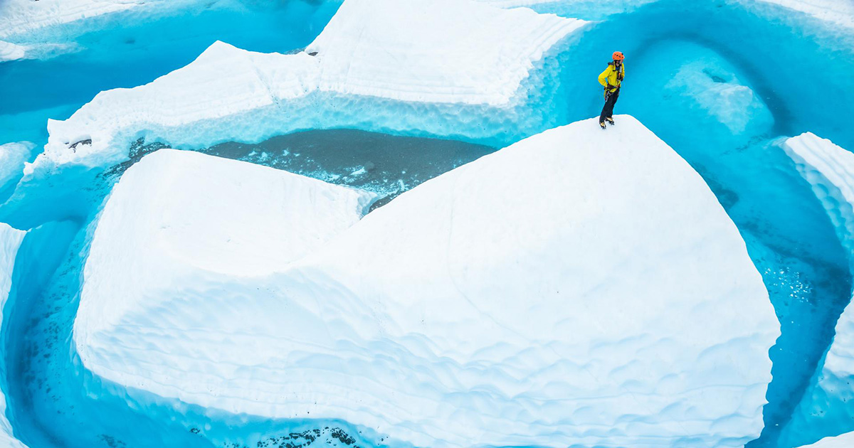 Stranded on a large ice fin, a man stands on top looking at the lake surrounding him.
