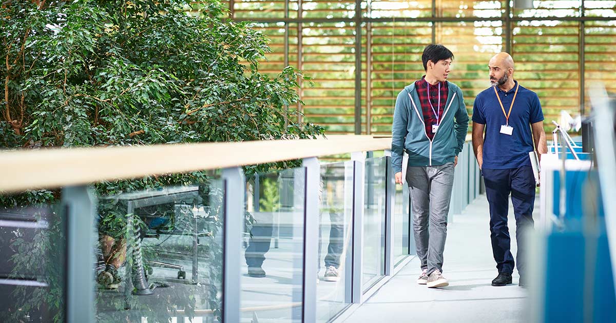 Two men walking through modern tech company lobby with large window and leafy plant, walk, two people, casual, diverse, tree, atrium