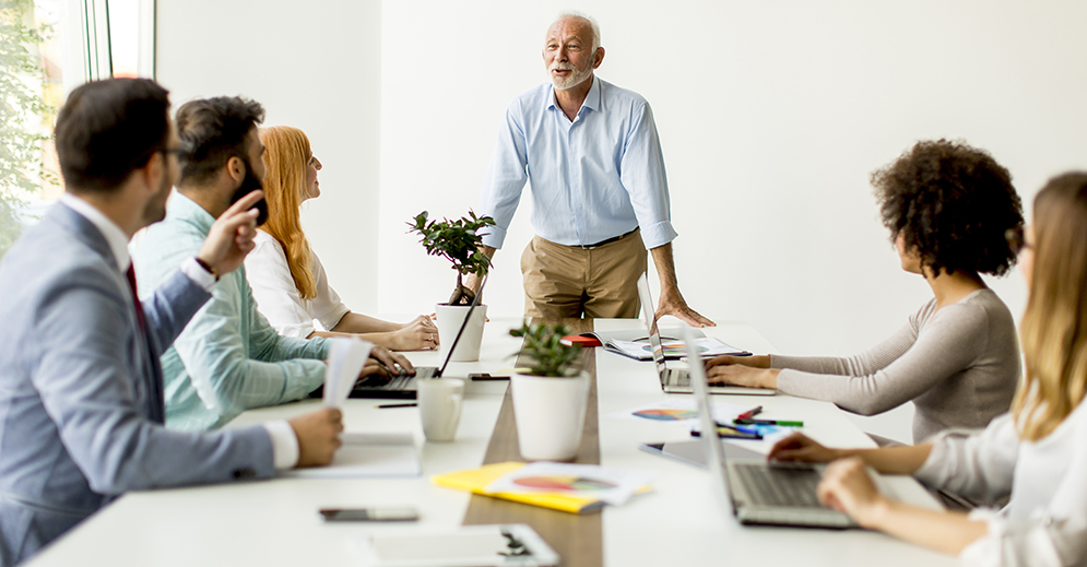 Senior businessman holds a meeting for younger colleagues, group, diverse, laptop, cup, conference room, man