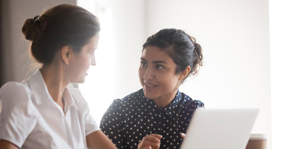 Senior female manager helping young smiling indian intern