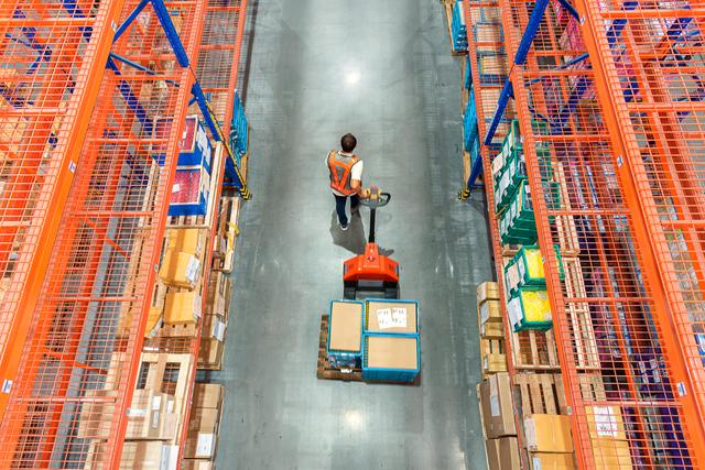 High angle view of Male warehouse worker pulling a pallet truck at distribution warehouse.