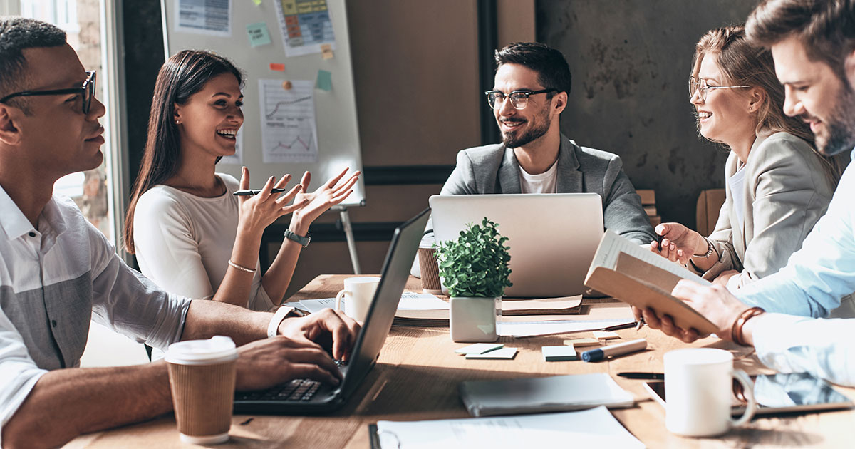 Working together. Group of young modern people in smart casual wear discussing business and smiling while sitting in the creative office