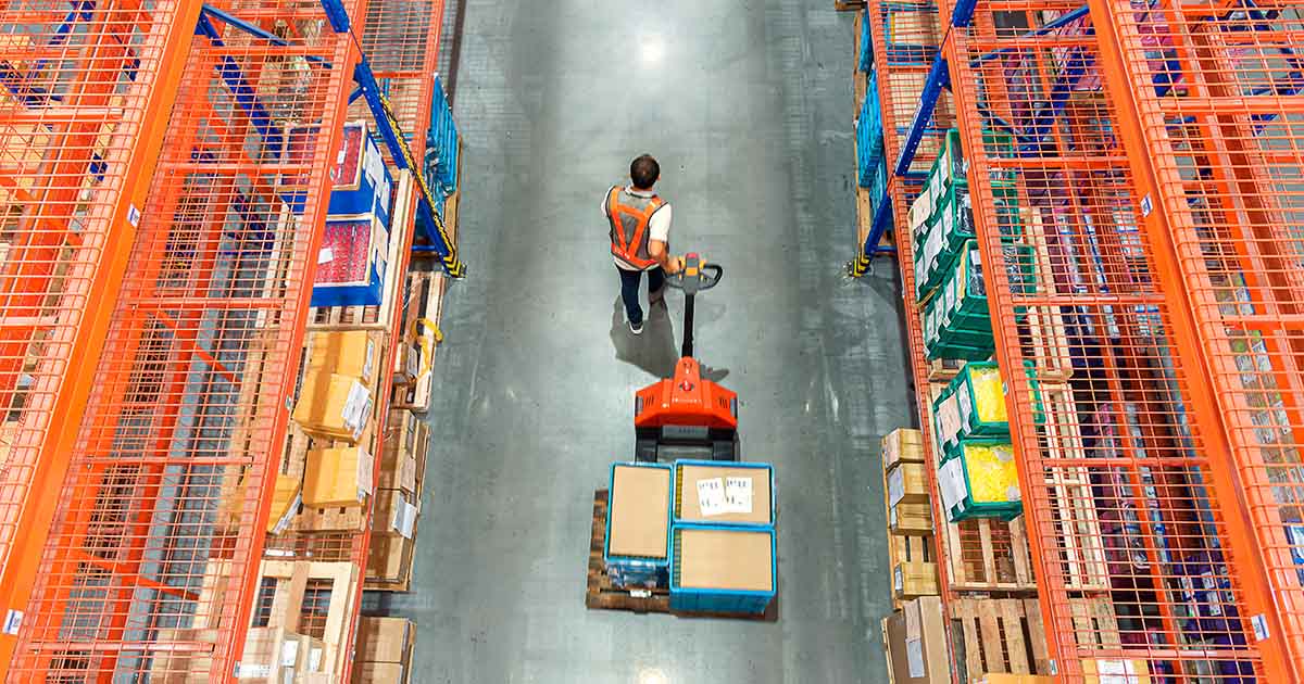 High angle view of Male warehouse worker pulling a pallet truck at distribution warehouse.