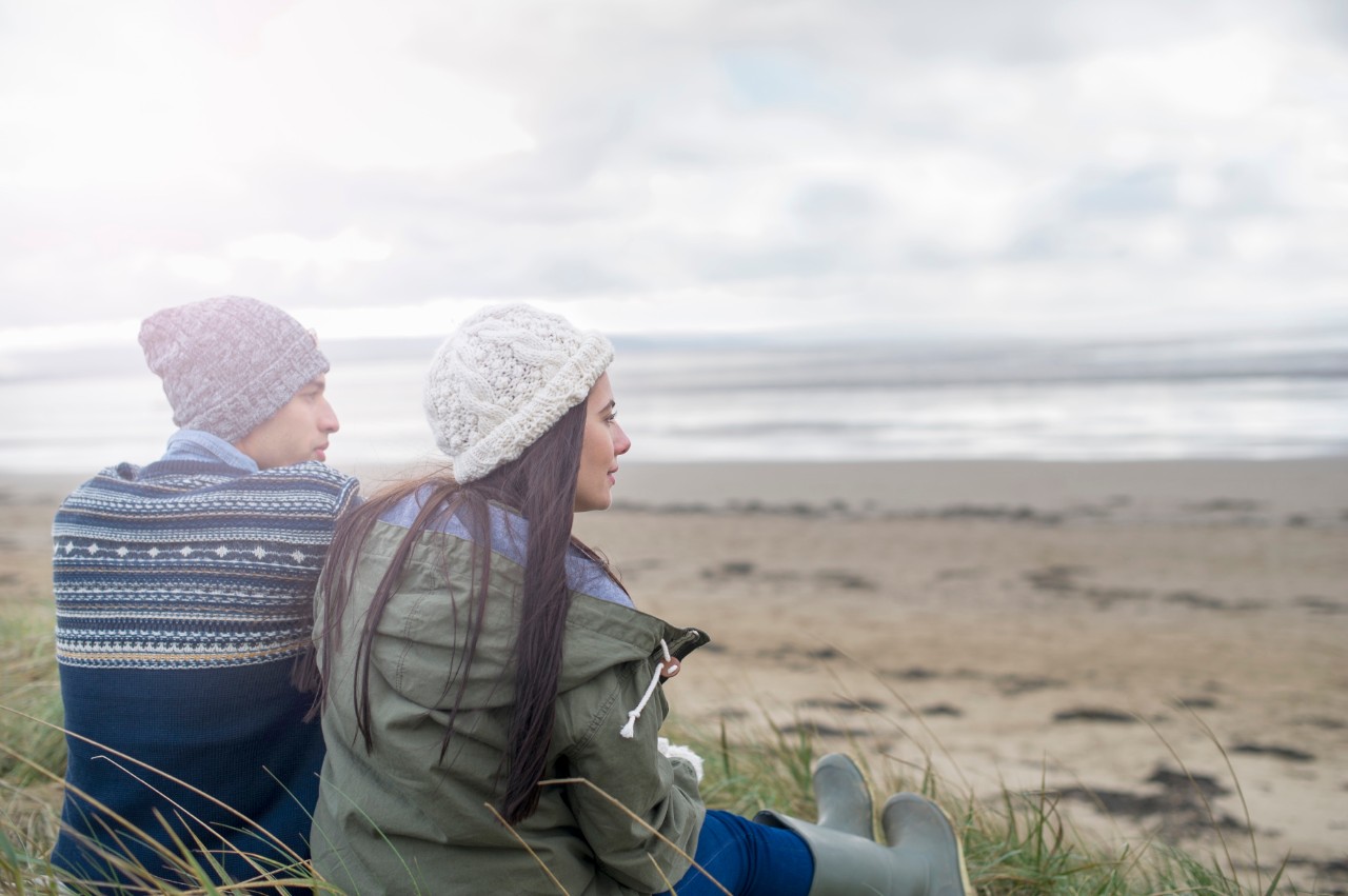 480812531 Young couple sitting on beach, Brean Sands, Somerset, England