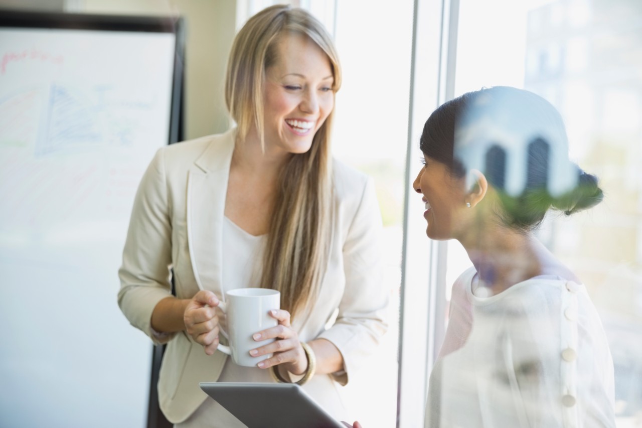 Smiling businesswomen with digital tablet talking in office