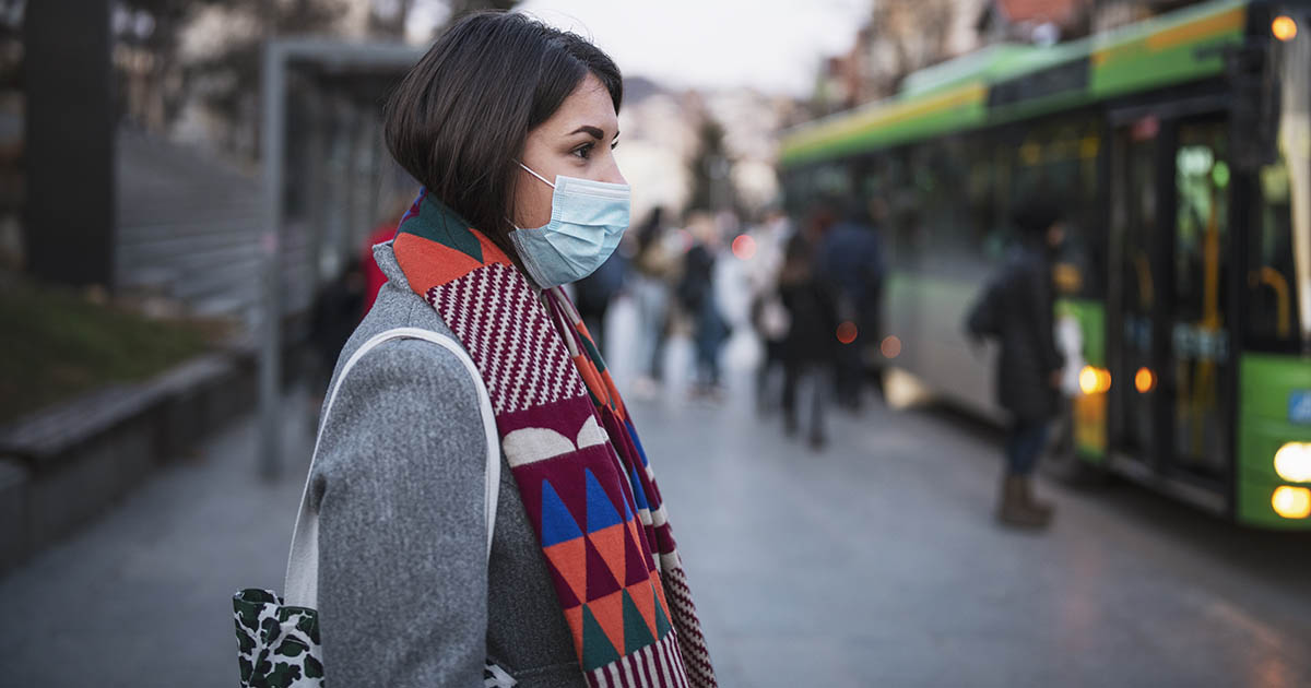 1204304023
Side view of young woman with protective face mask in town, she standing in front at the bus stop and waiting for her transport after work.