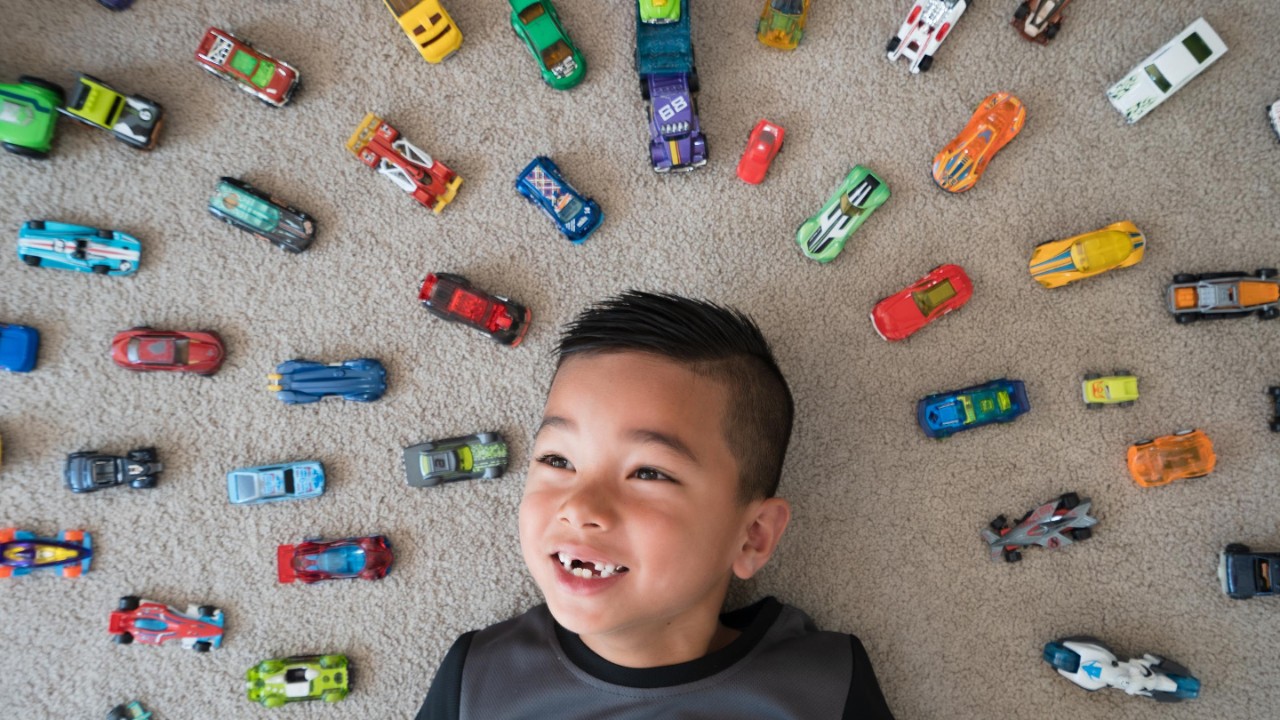 Kid at home lying on ground with cars around him