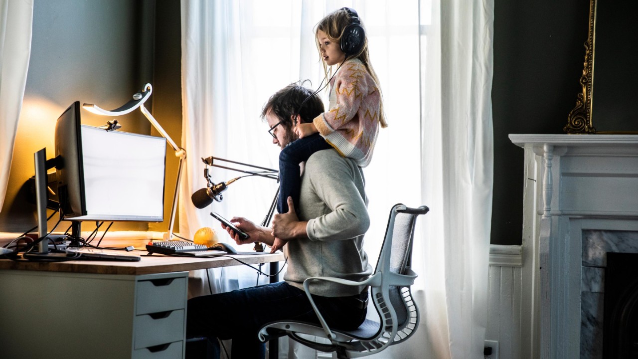 Padre trabajando en la oficina en casa con su hija sobre los hombros