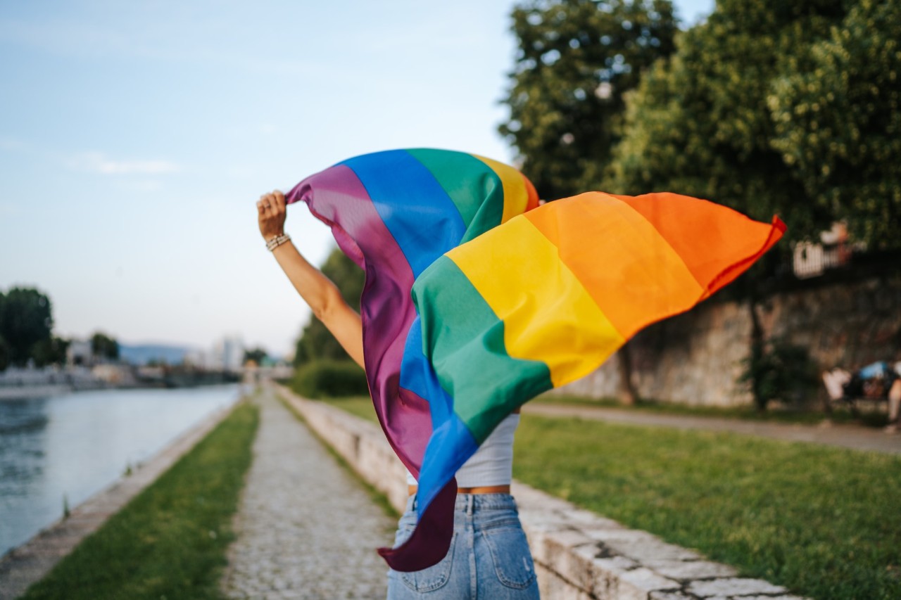 Una persona corriendo con una bandera del Orgullo al otro lado del río
