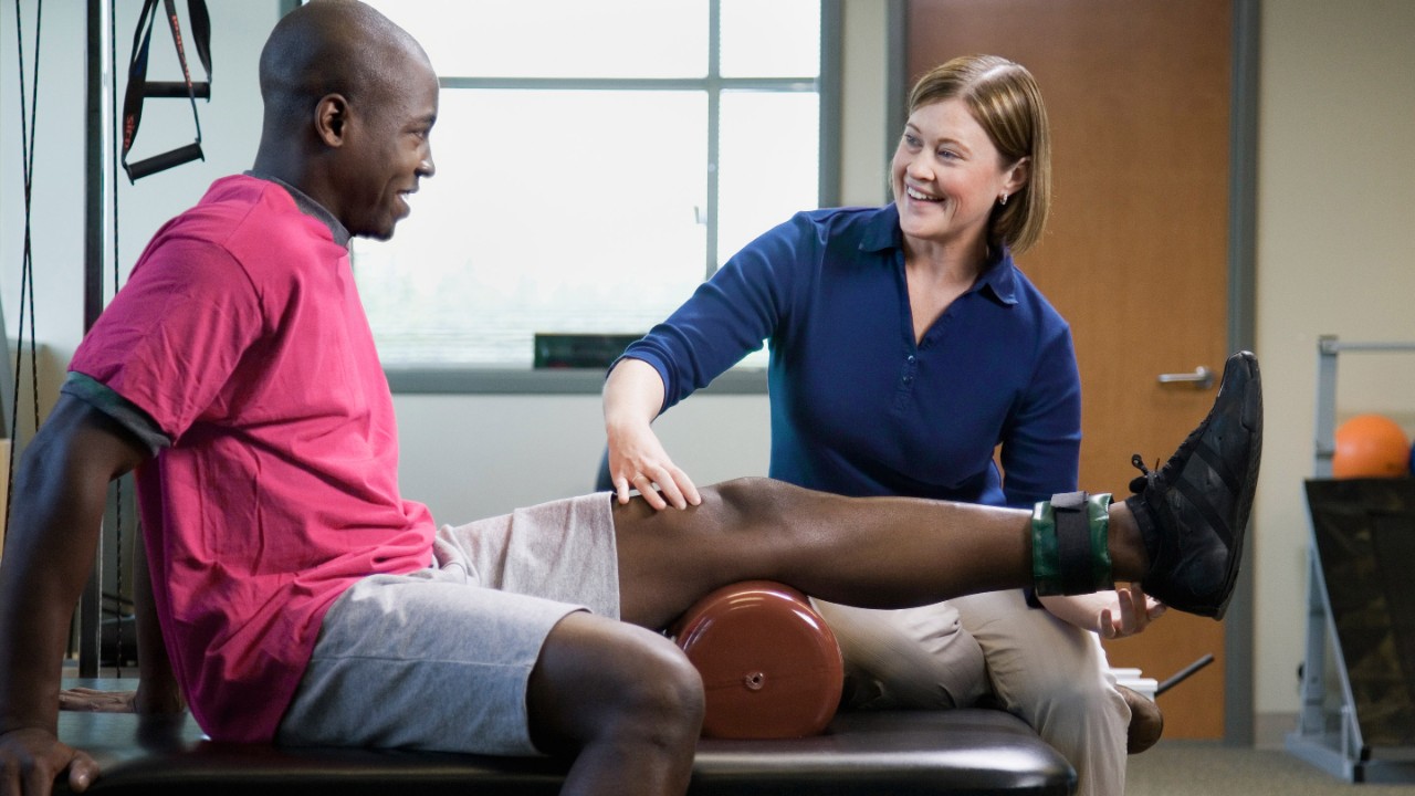 Female physical therapist assisting man with leg exercise