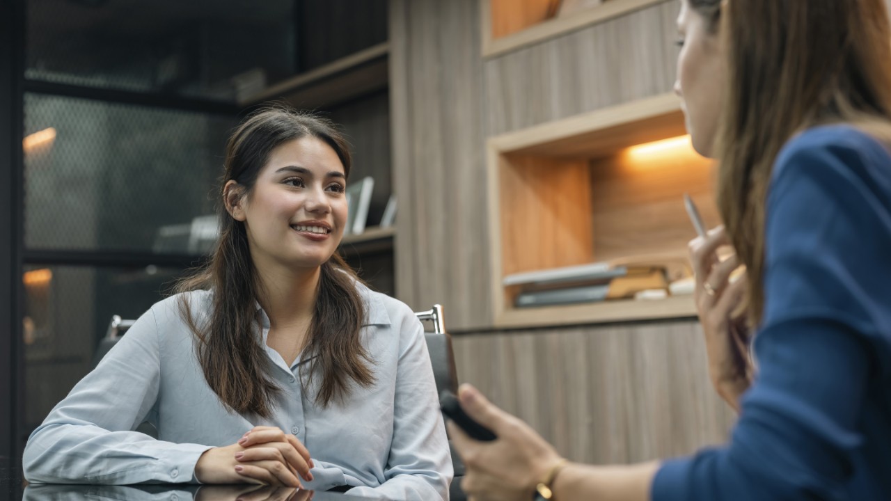 Recruiter holding candidate resume taking job interview at desk. HR female manager talking with candidate during job interview in office. Woman sitting in board room and taking business interview of a female interviewee.
