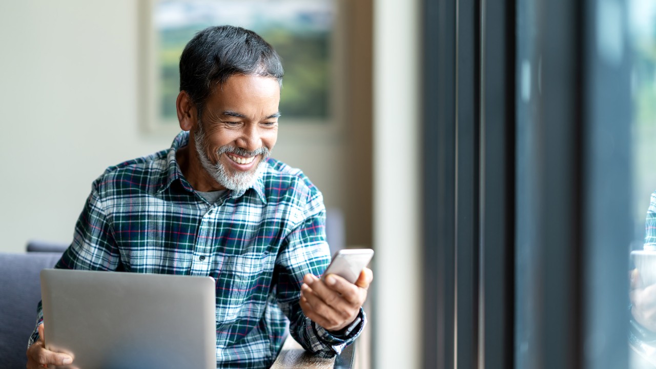 Un homme assis sourit au téléphone avec un ordinateur portable sur ses genoux