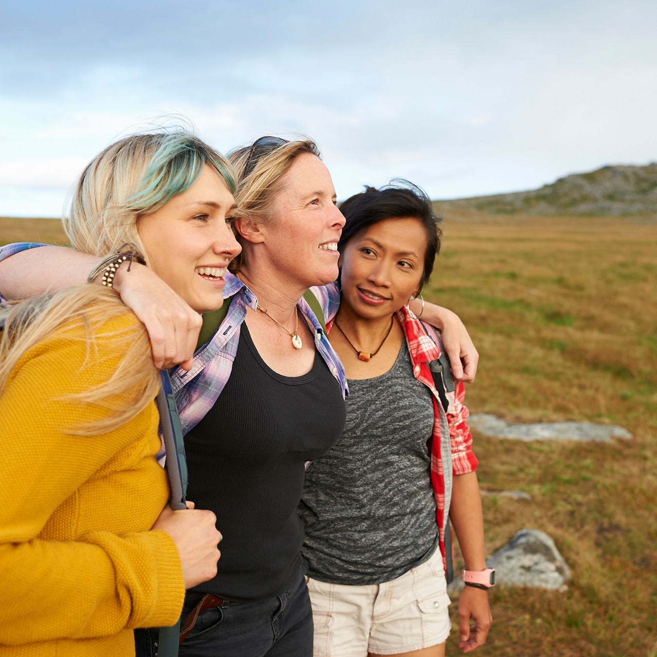 A group of happy and positive female hiking friends huddle together on a rocky moorland in an idyllic rural countryside.