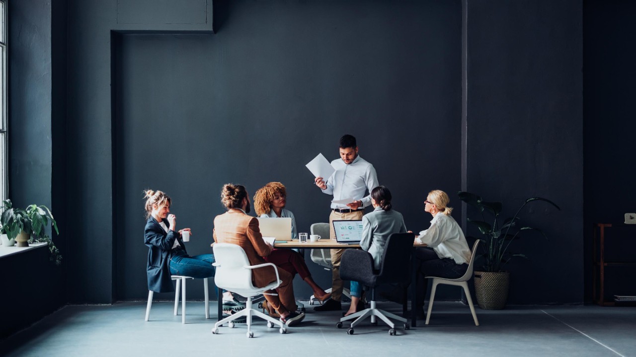 Equipo multiétnico de seis hombres y mujeres de negocios felices que analizan ideas juntos durante una reunión informal en la oficina.