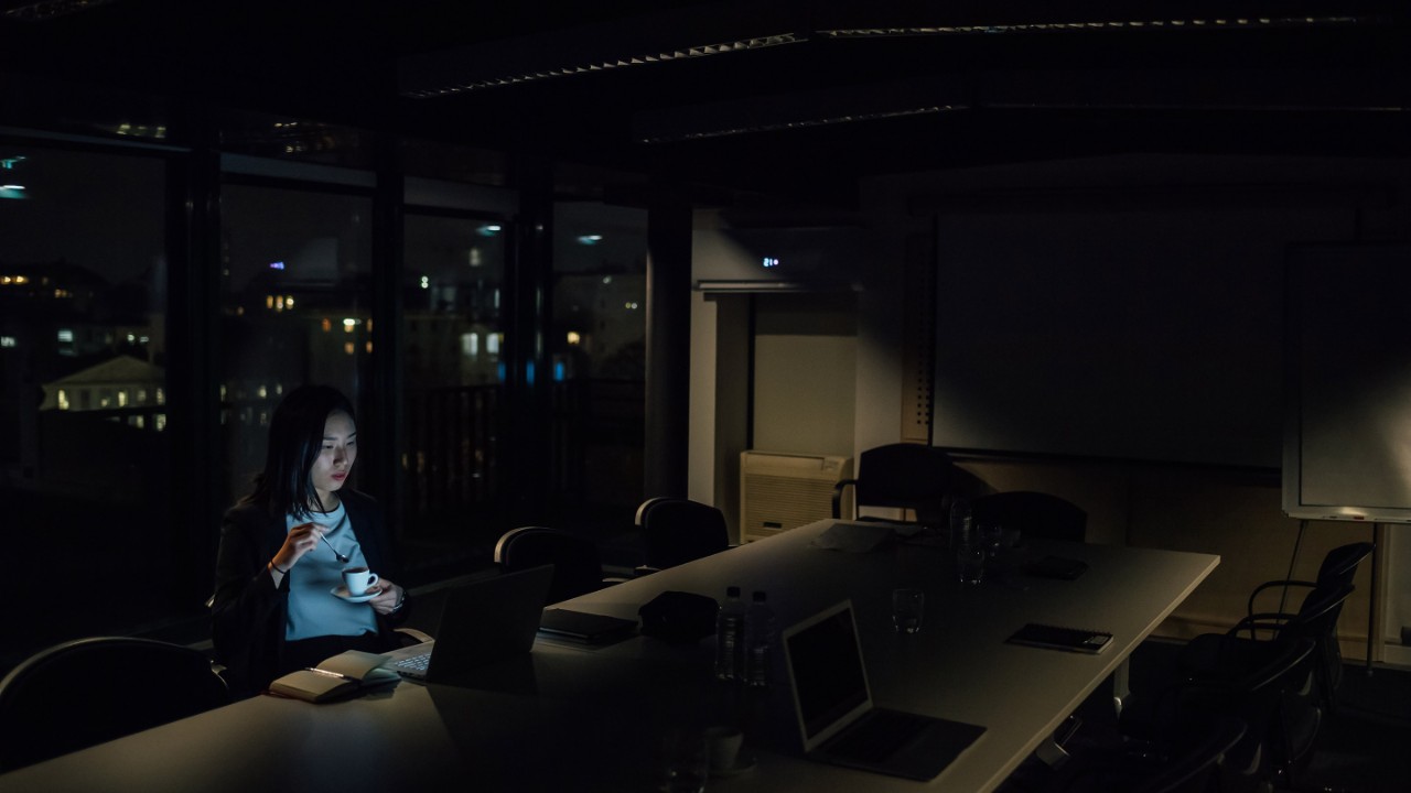 Young businesswoman in office at night looking at laptop