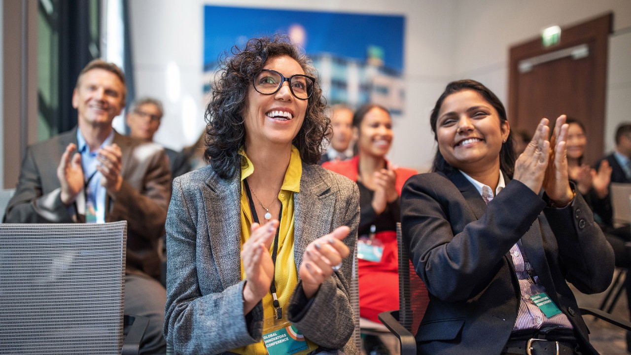 Multi-ethnic business people clapping while sitting in auditorium during seminar. Professionals applauding in a launch event at convention center.