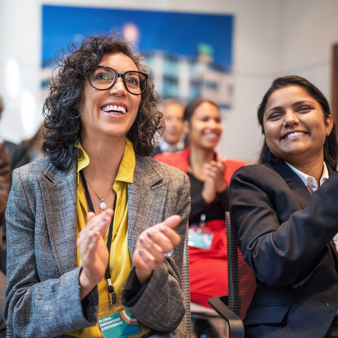Multi-ethnic business people clapping while sitting in auditorium during seminar. Professionals applauding in a launch event at convention center.
