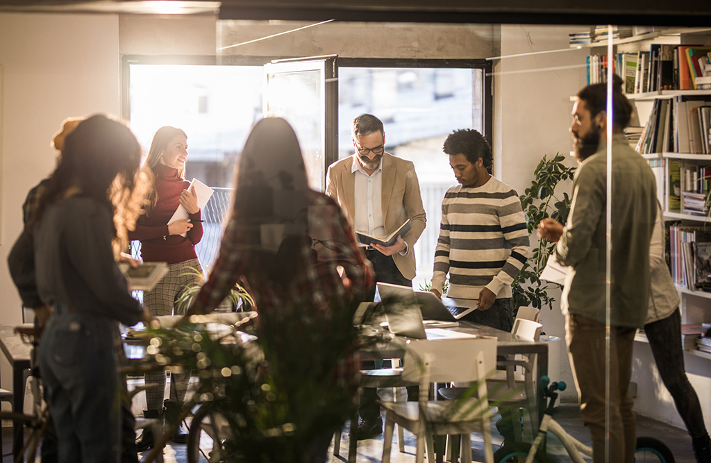 Group of multi-tasking creative people working on a meeting in the office. The view is through glass.