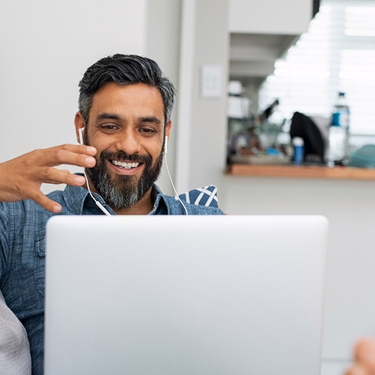 Happy mature man relaxing on couch while video calling using laptop at home. Latin man sitting on sofa and making a video call. Smiling middle eastern businessman doing online video chat while gesturing with hands.
