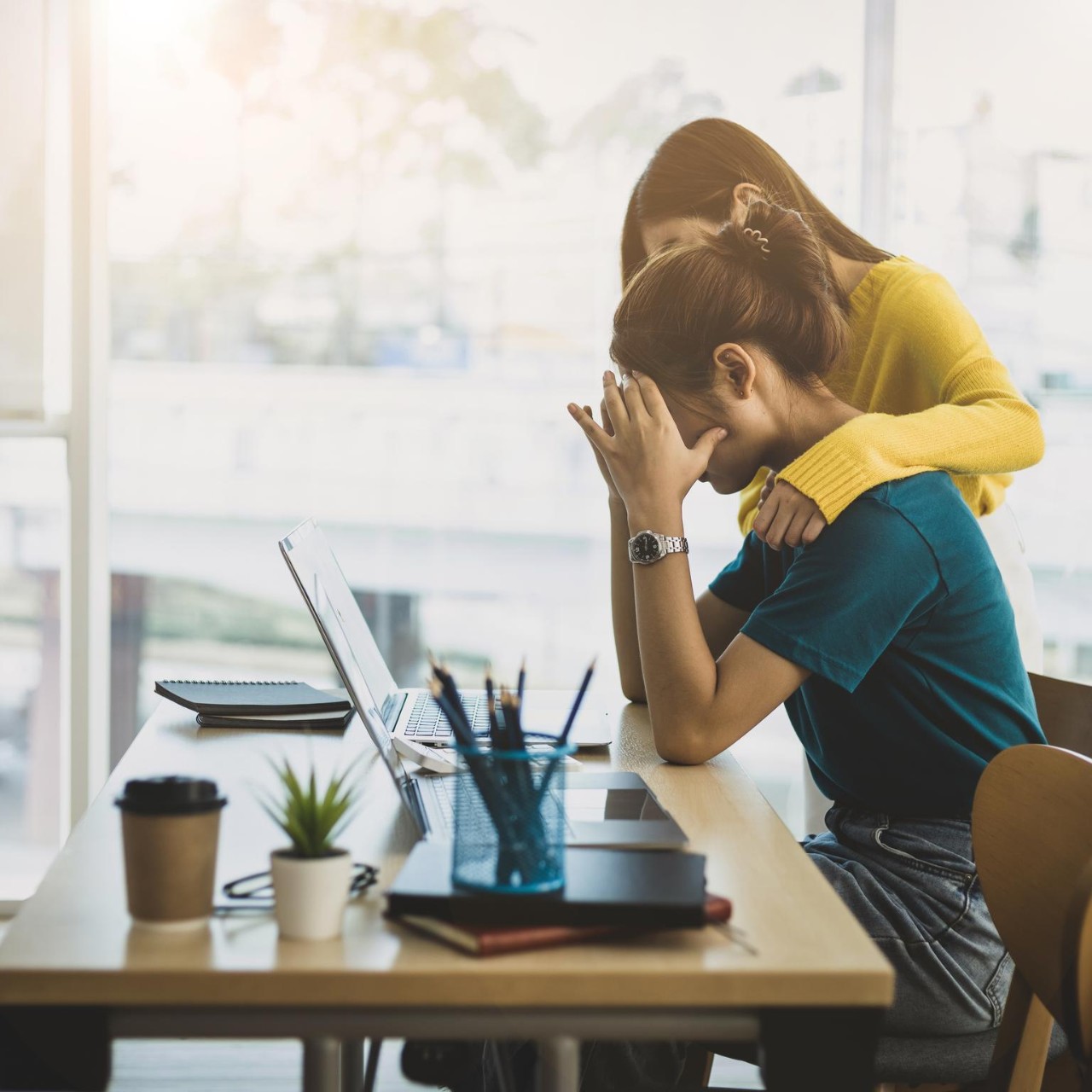 Coworker comforting stressed and discouraged woman in office.
