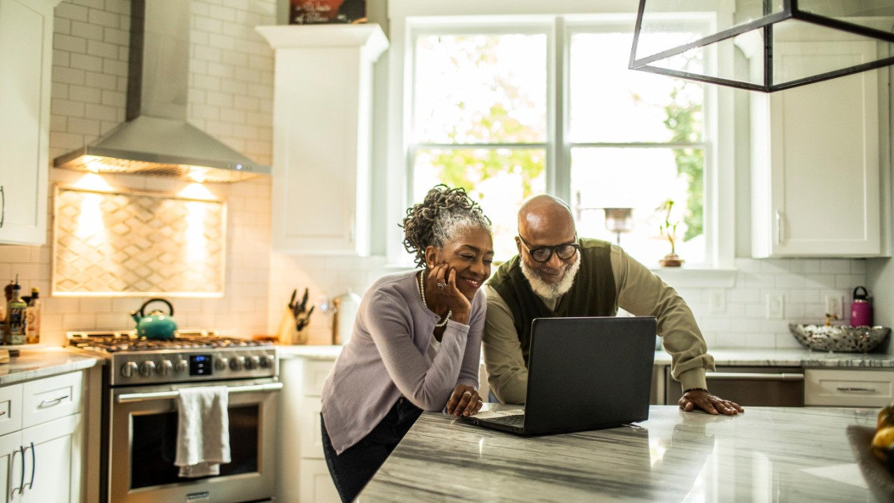 Senior couple using laptop in kitchen of suburban home