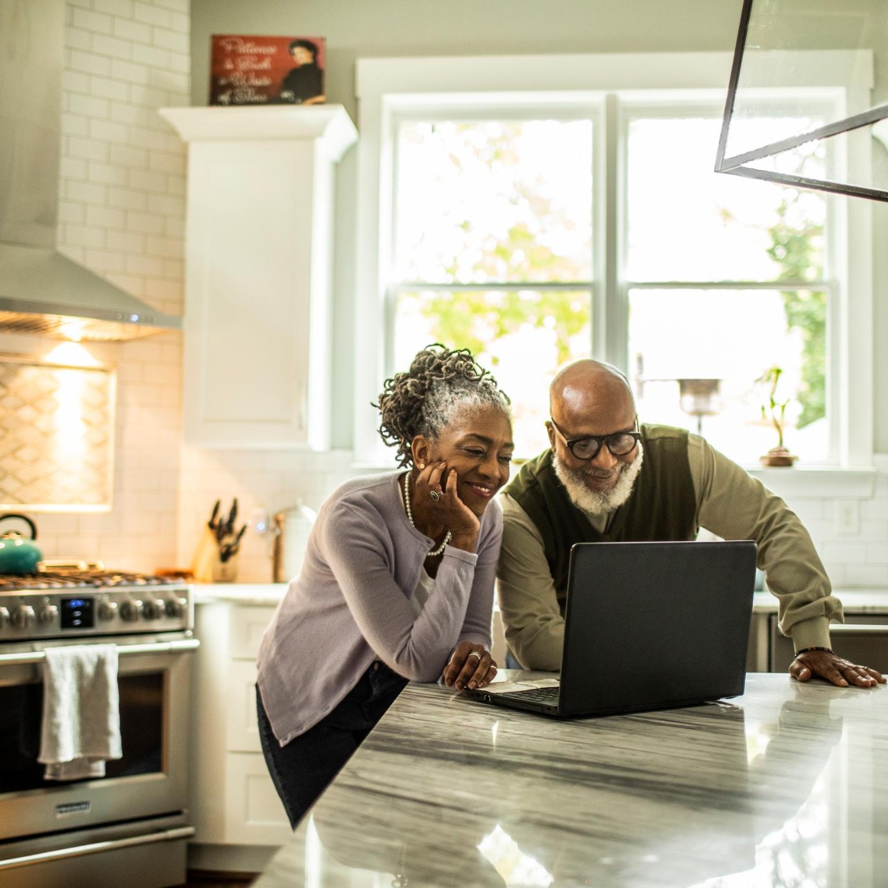 Senior couple using laptop in kitchen of suburban home