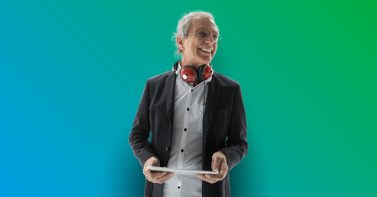 Smiling elderly man standing holding a tablet with headphones around neck - Blue to green gradient