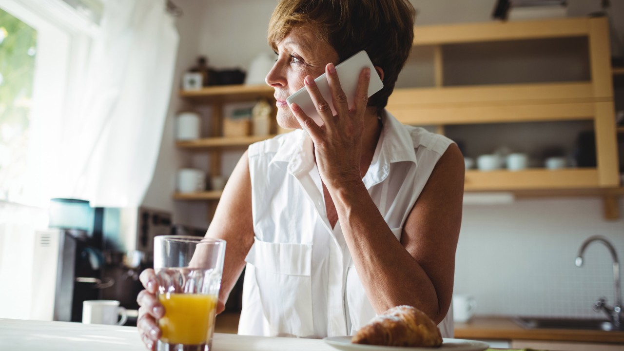 Senior woman talking on phone while having breakfast