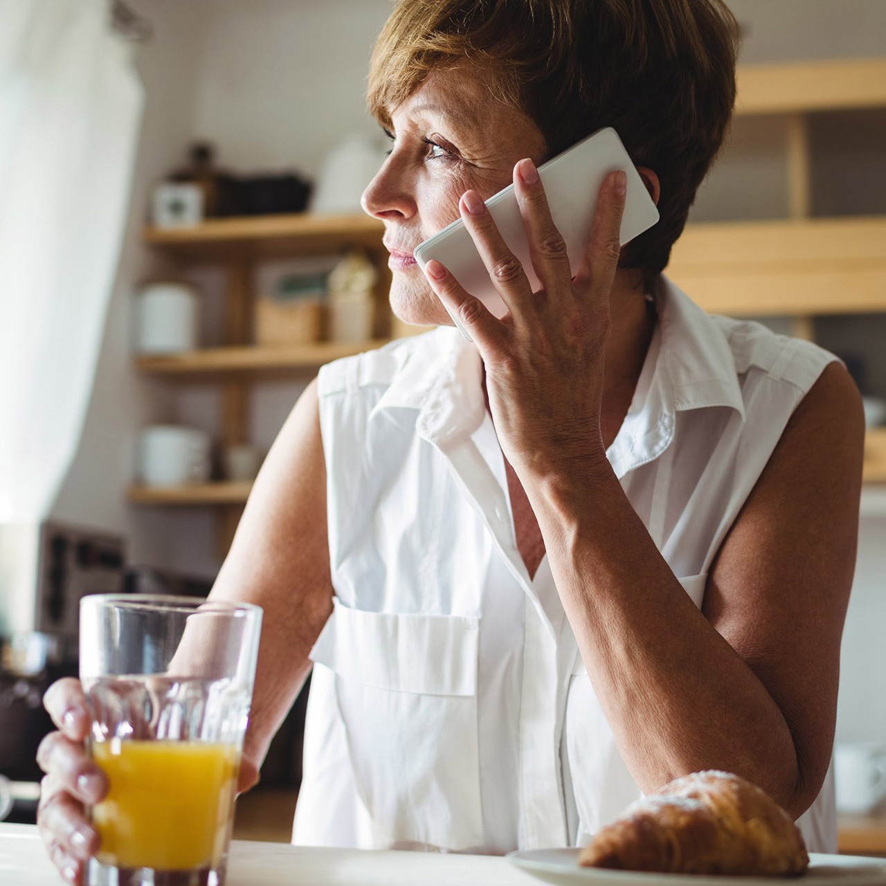 Senior woman talking on phone while having breakfast