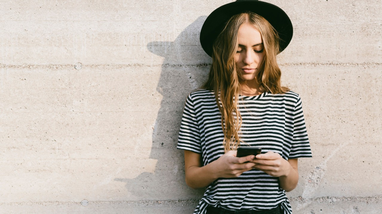 Portrait of fashionable young woman wearing hat using smartphone