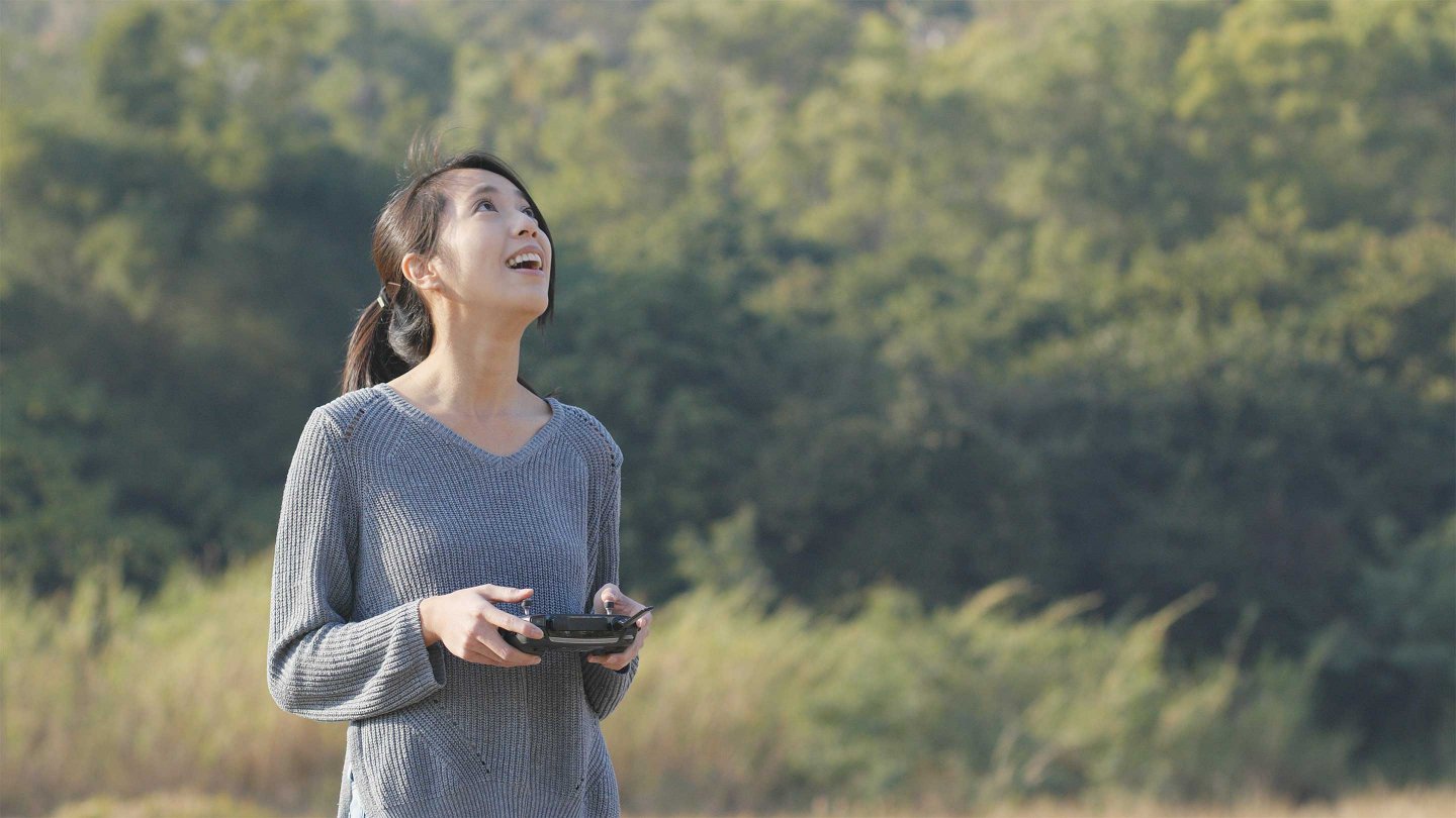 Woman controling flying drone in the park 