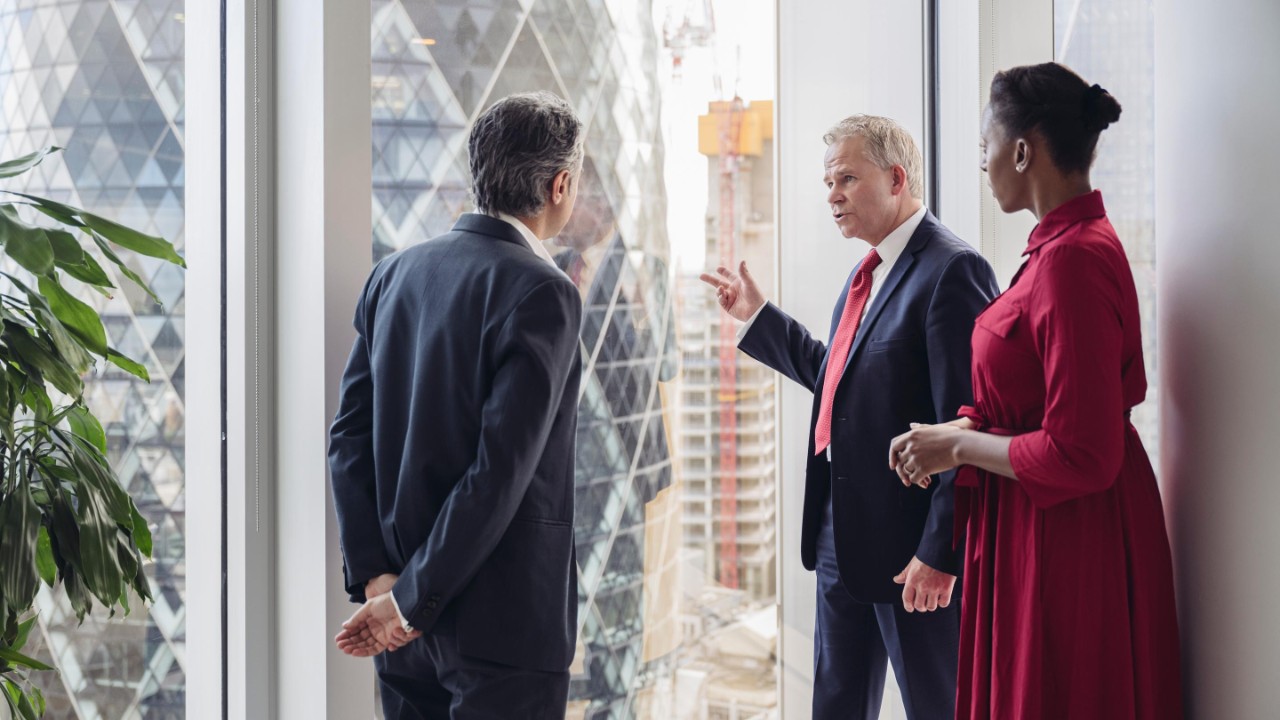 Male and female businesspeople standing at full length window of modern office building