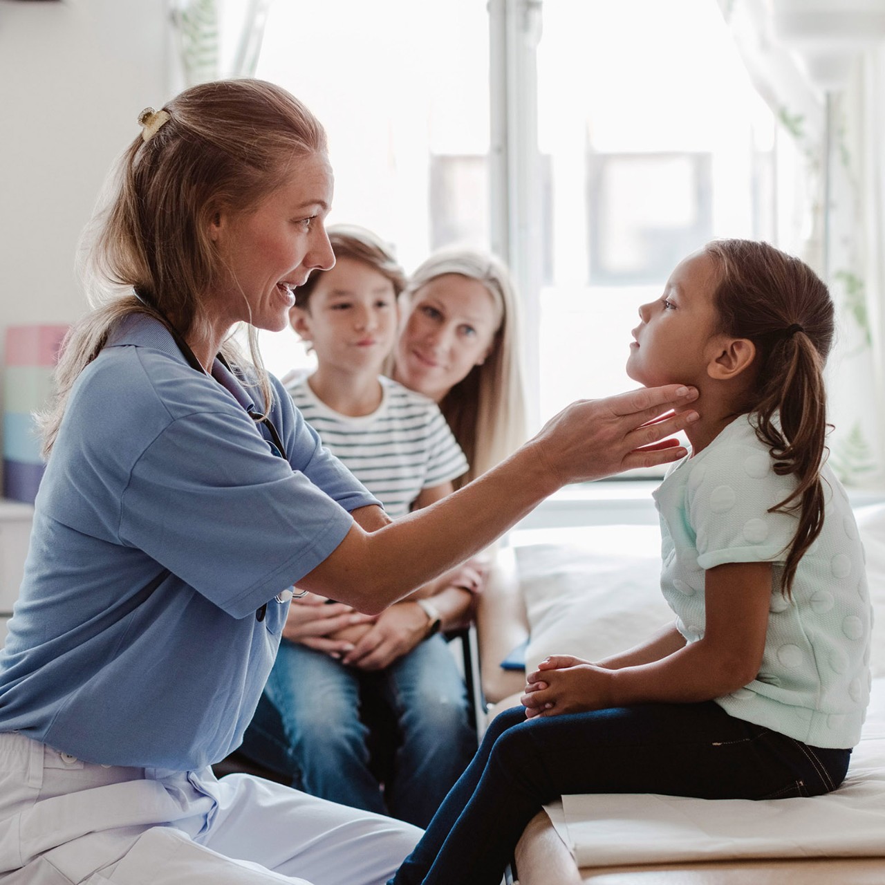 doctor treating small girl while mother and son look on