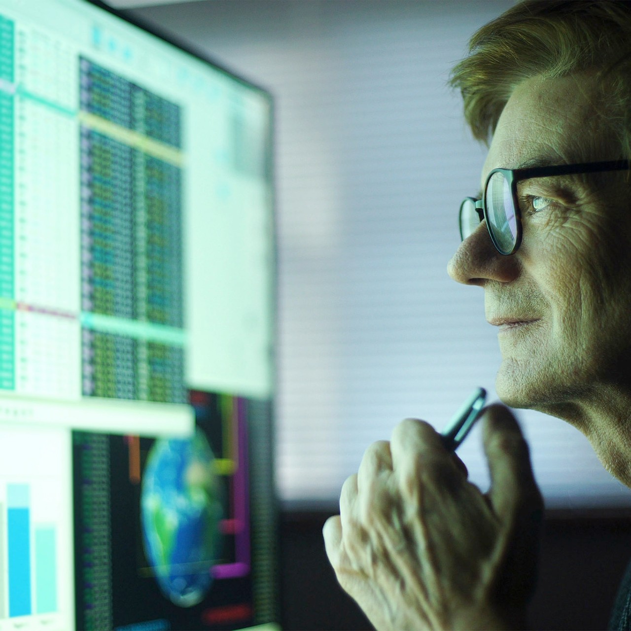 Stock photo of a mature man working in his home office. Heâ  s studying a large computer monitor displaying a variety of numerical data, global information & text.