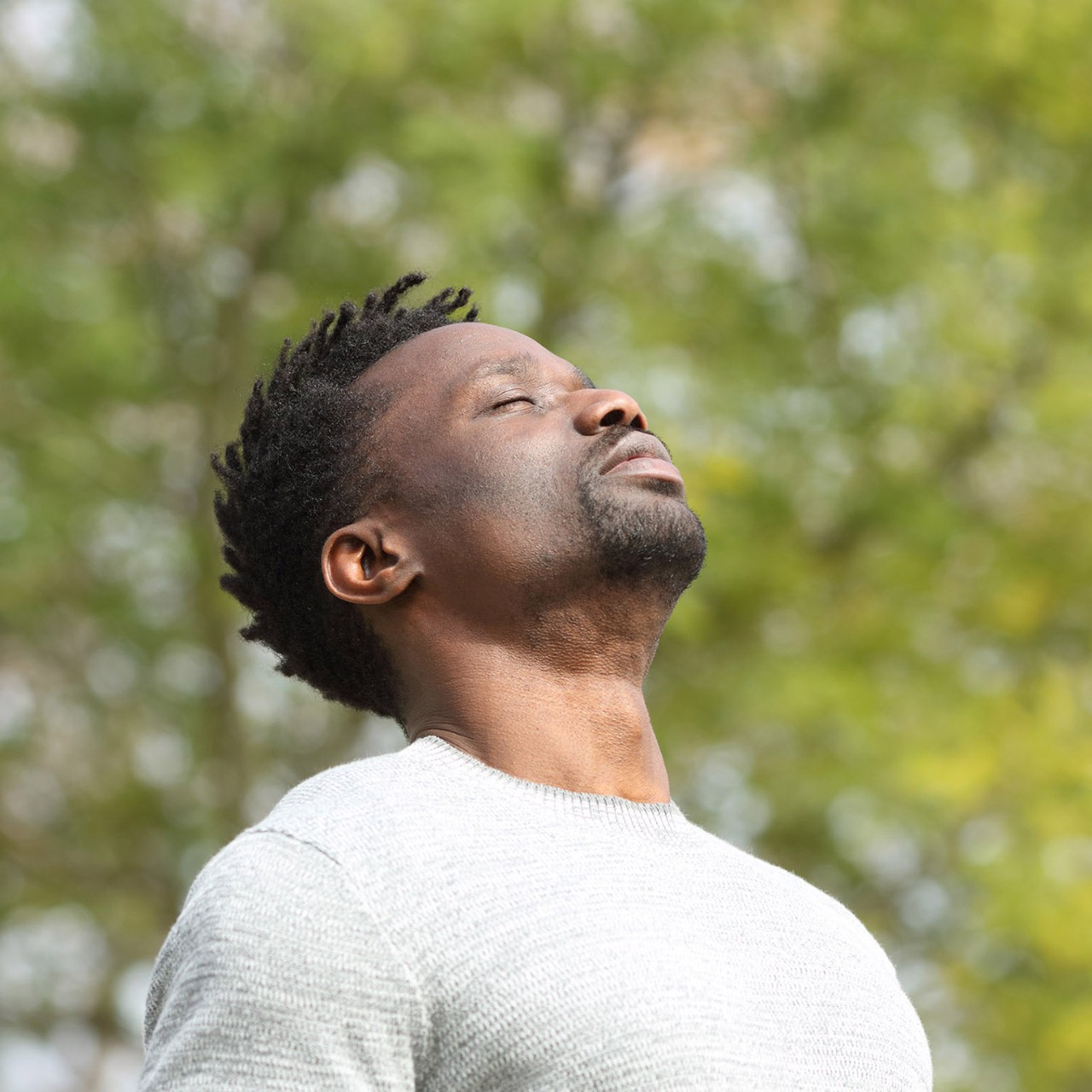Black serious man breathing deeply fresh air in a park a sunny day with a green tree in the background