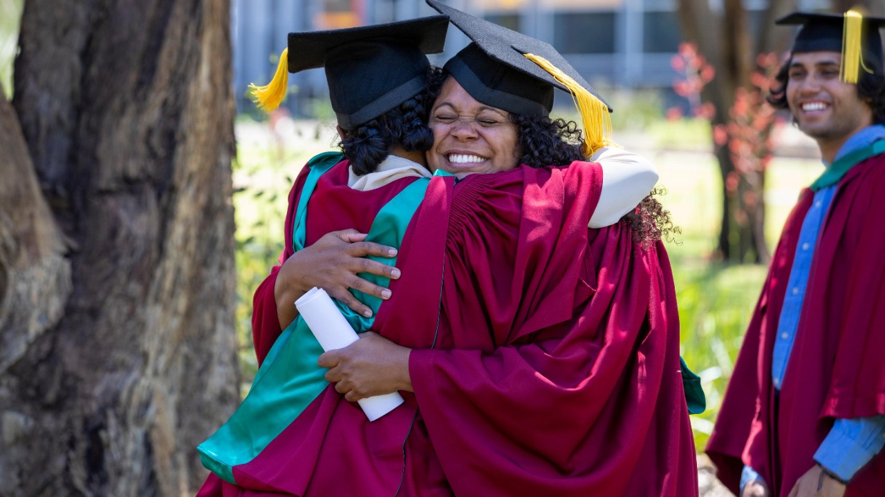 Young aboriginal students cuddling each other dressed in their graduation gowns.