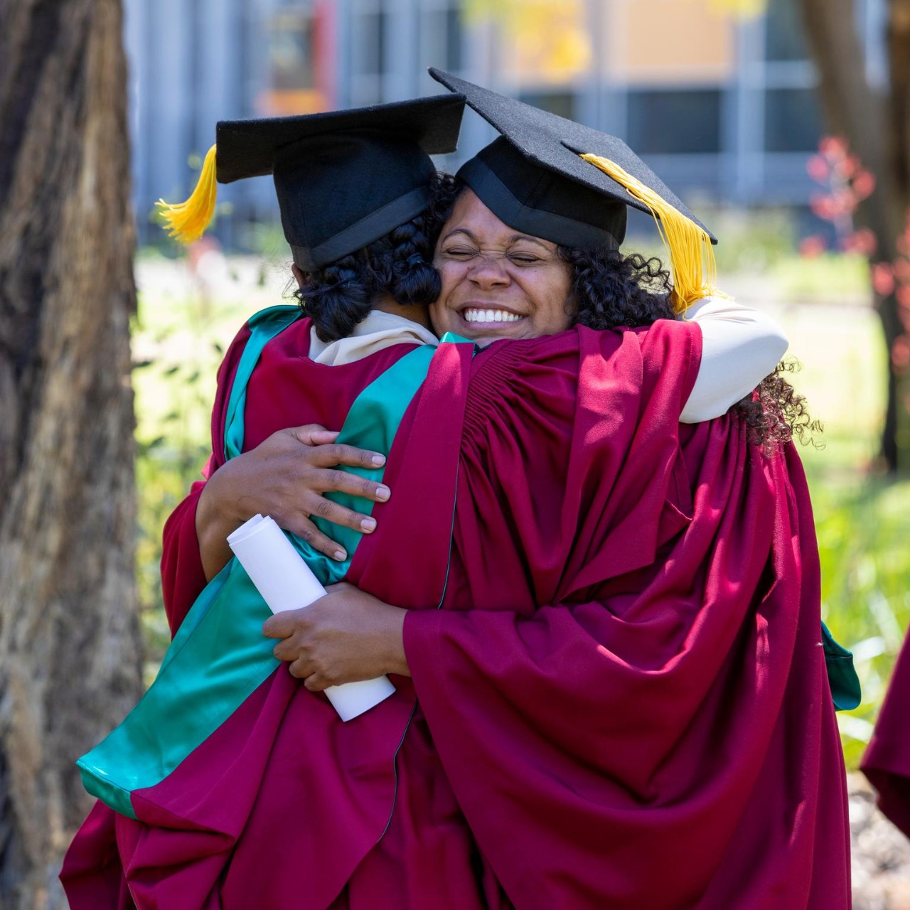 Young aboriginal students cuddling each other dressed in their graduation gowns.