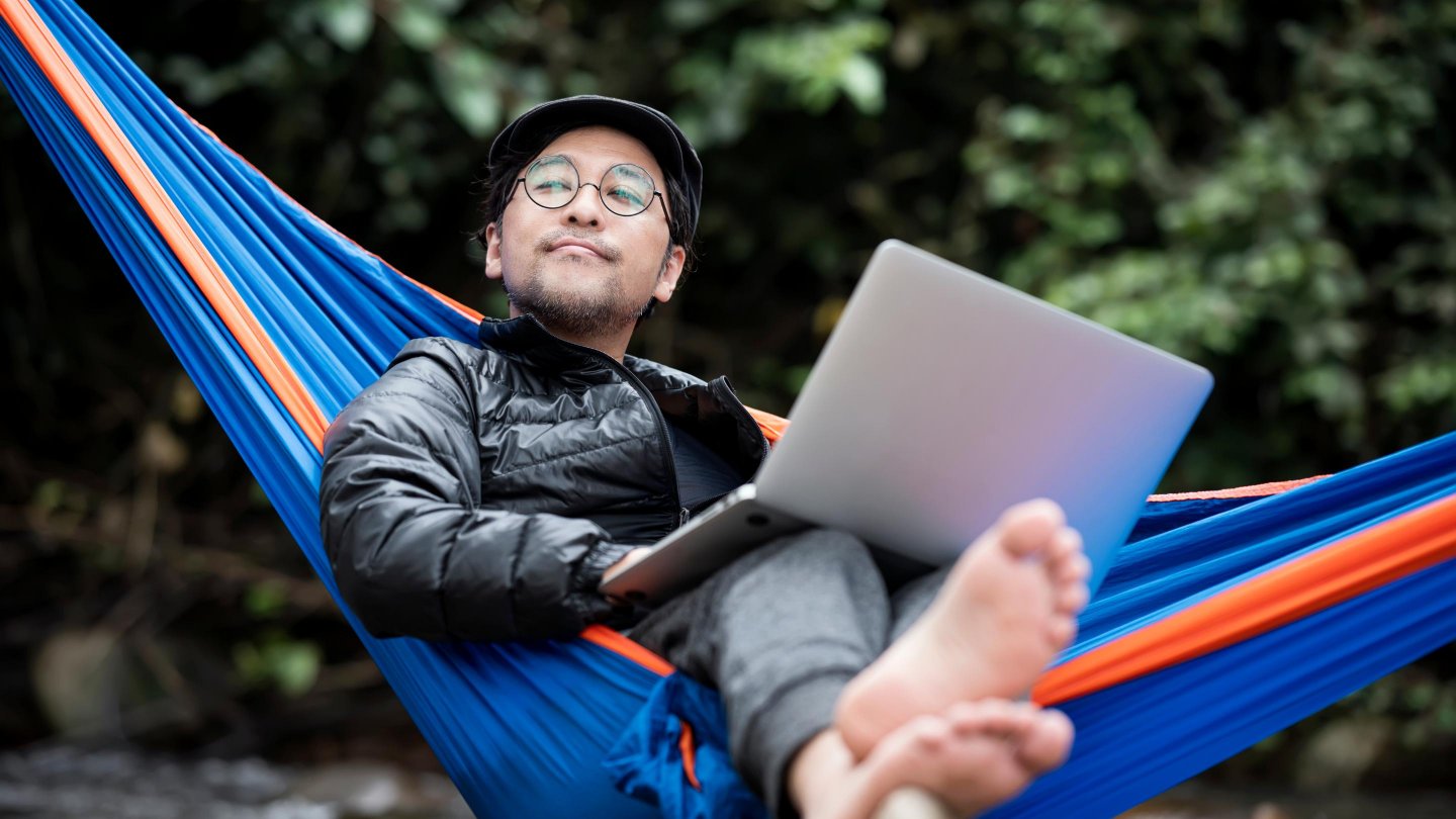 Senior Man lying in hammock using a laptop on a vacation