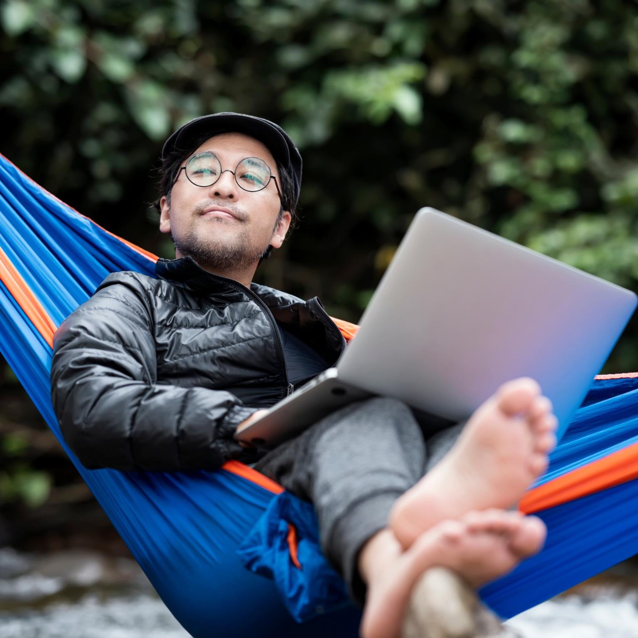 Senior Man lying in hammock using a laptop on a vacation