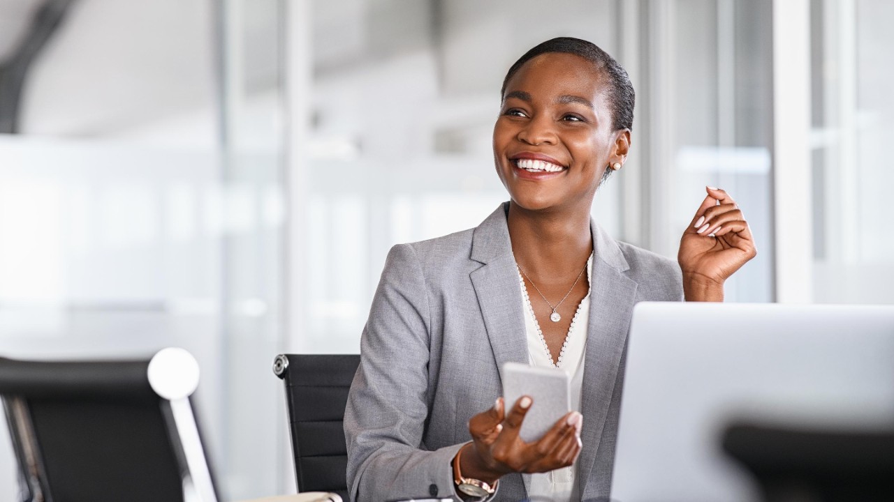 African black business woman using smartphone while working on laptop at office