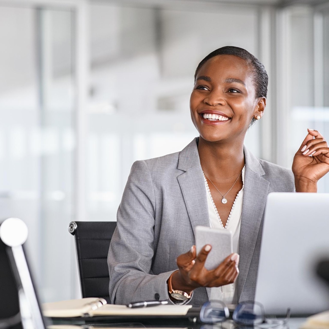 African black business woman using smartphone while working on laptop at office
