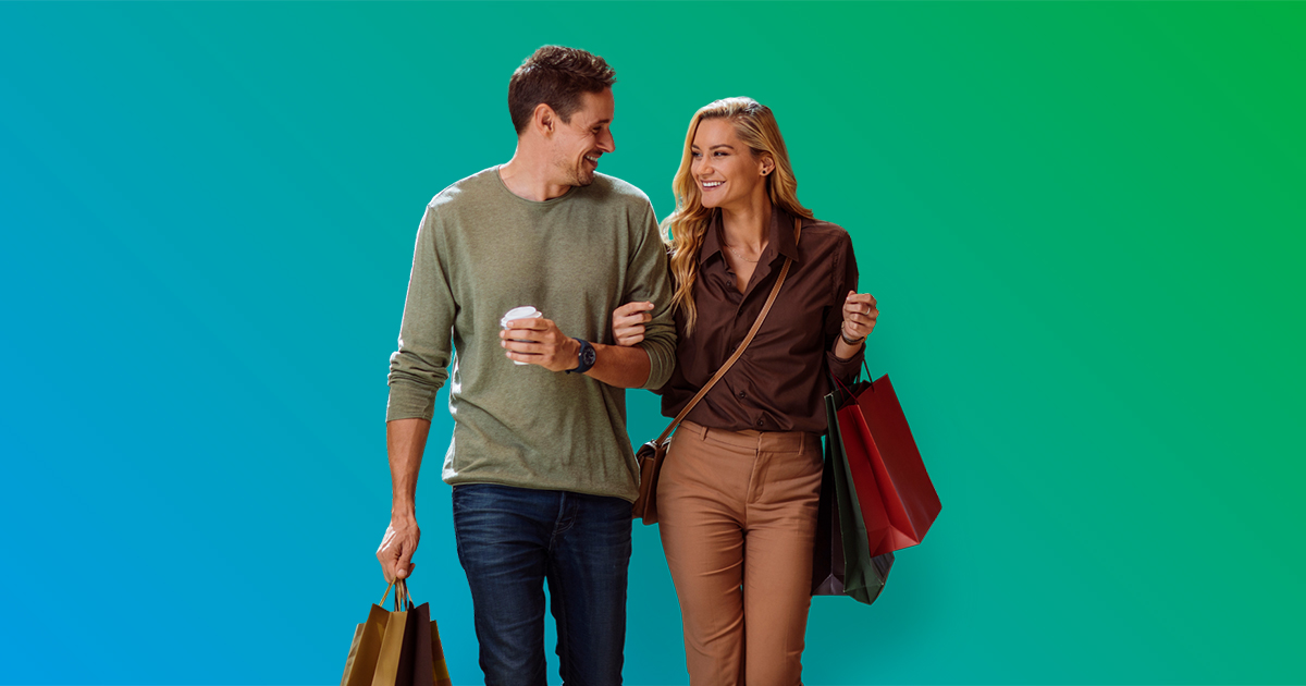 Couple walking with arms linked carrying shopping bags and coffee cup - blue to green gradient