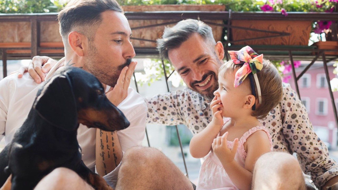 Happy gay couple with daughter and dog on balcony
