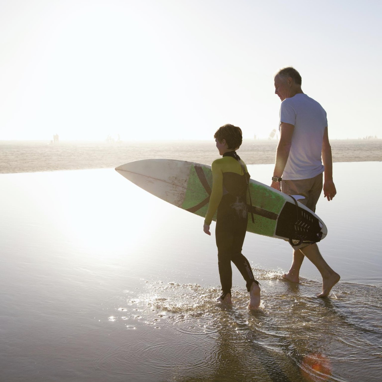 Man walking with his grandson towards a place to surf on a beach