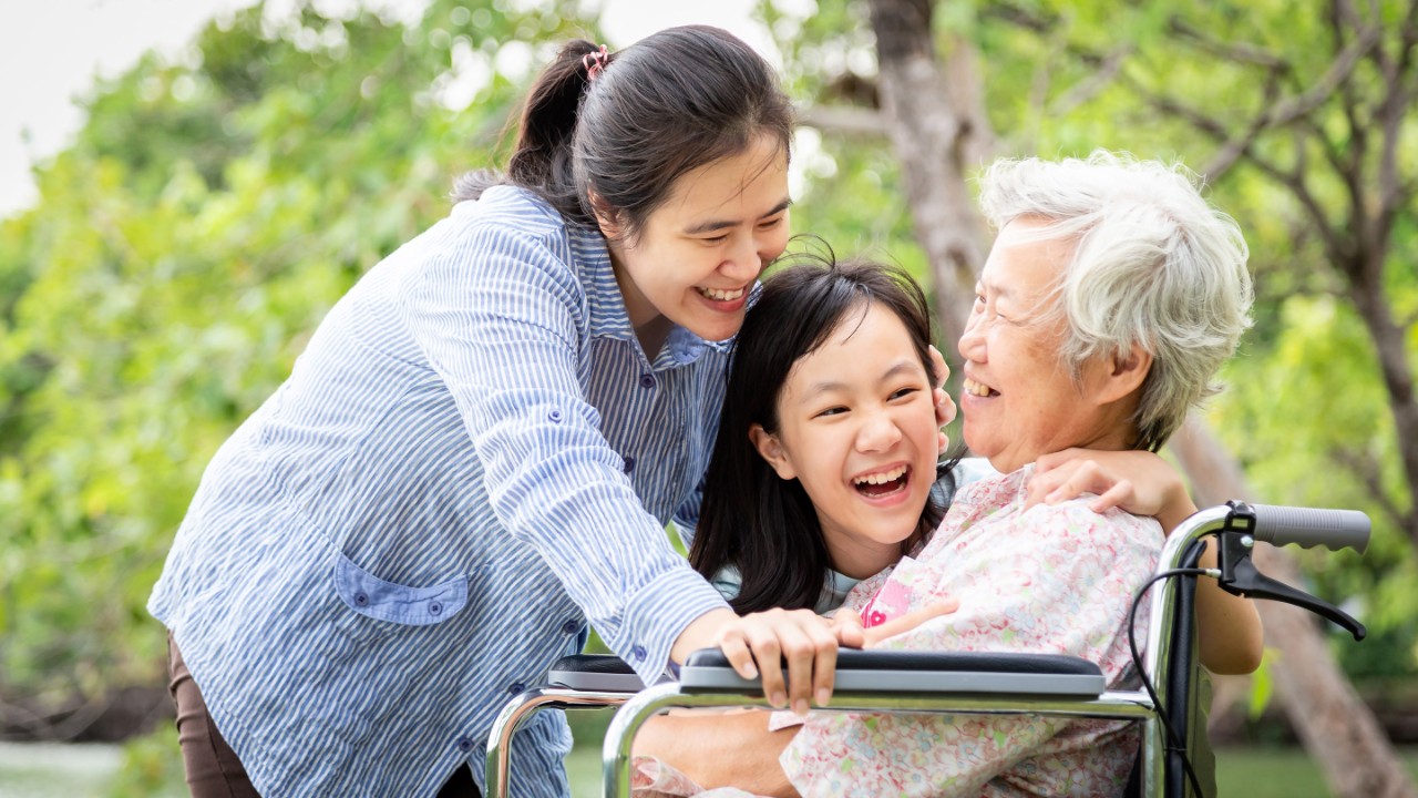 Asian family,senior grandmother,mother,smiling daughter enjoy,hugging in outdoor park,patient elderly people laughing talk funny with family in wheelchair,happy woman and little child girl care with her,love,relationship,health care concept