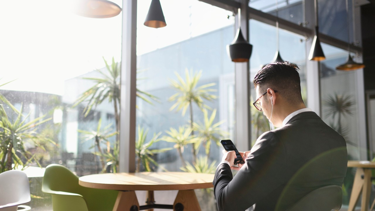 1148950342 Uomo in abito che lavora dal telefonoe ascolta musica con gli auricolari