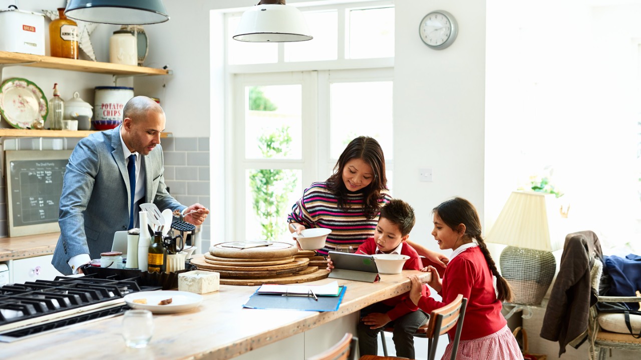 忙しい近代的な家族が仕事や学校の準備をし、朝食を食べる男性、オンラインで男の子と女の子を助ける母親