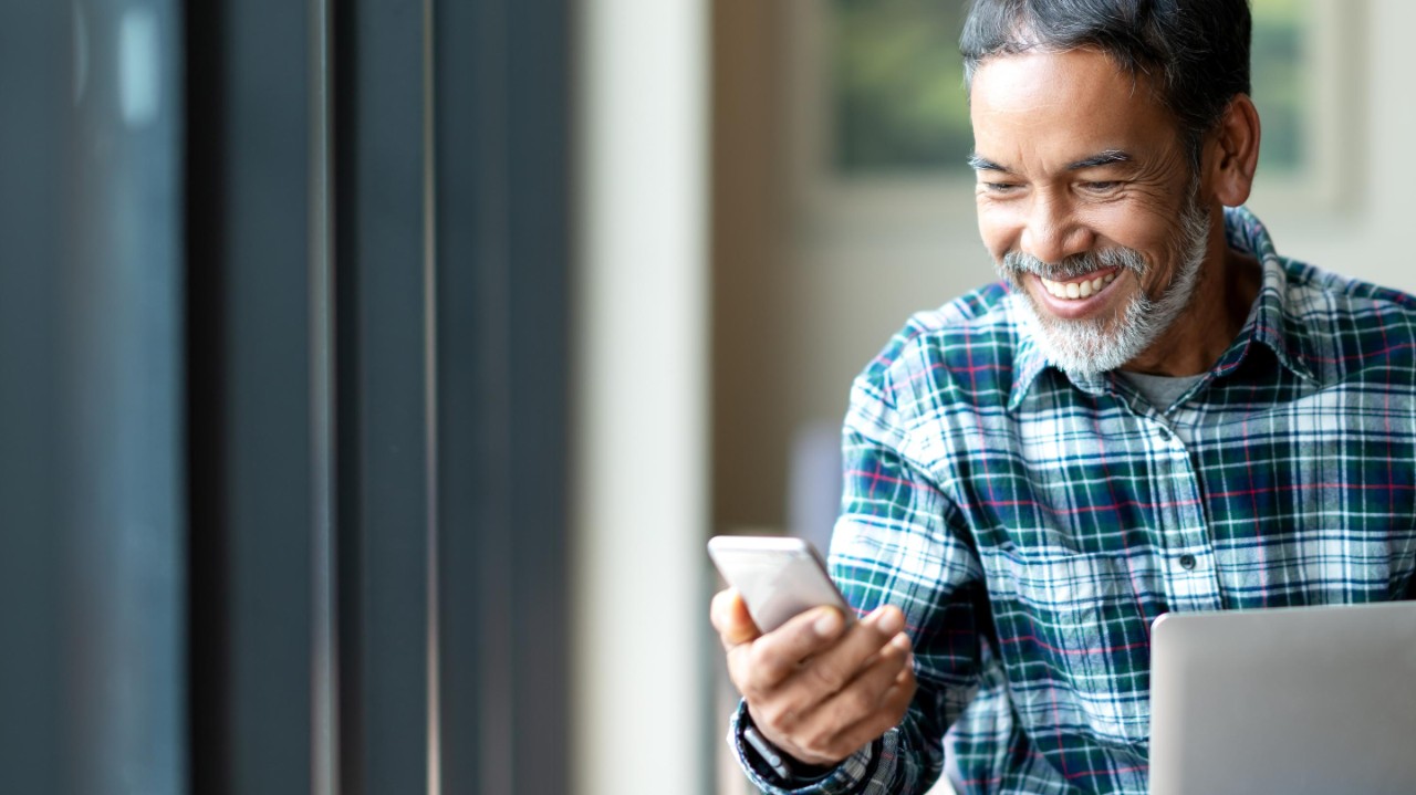 happy mature asian or hispanic old man looking at smartphone smiling positive in casual lifestyle with digital technology of older or senior guy concept. Urban elderly Asian retired man
