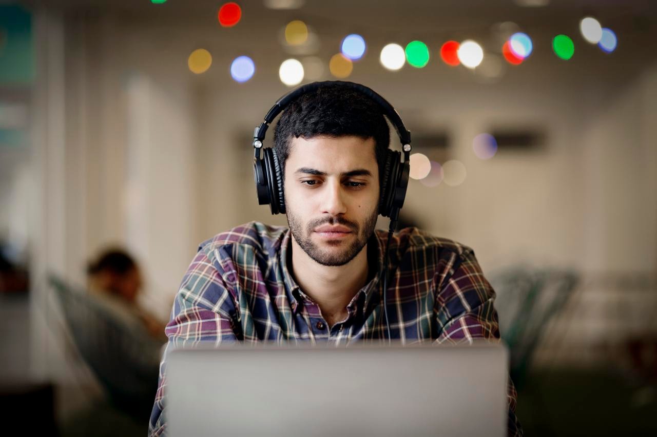  Businessman wearing headphones while working late on laptop in creative office クリエイティブ ・ オフィスのラップトップで遅くまで働いている間ヘッドフォンを身に着けているビジネスマン
